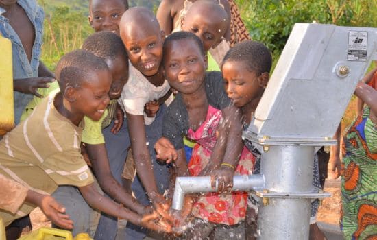 Children eagerly get water from a new well in Uganda, thanks to the Village Drill